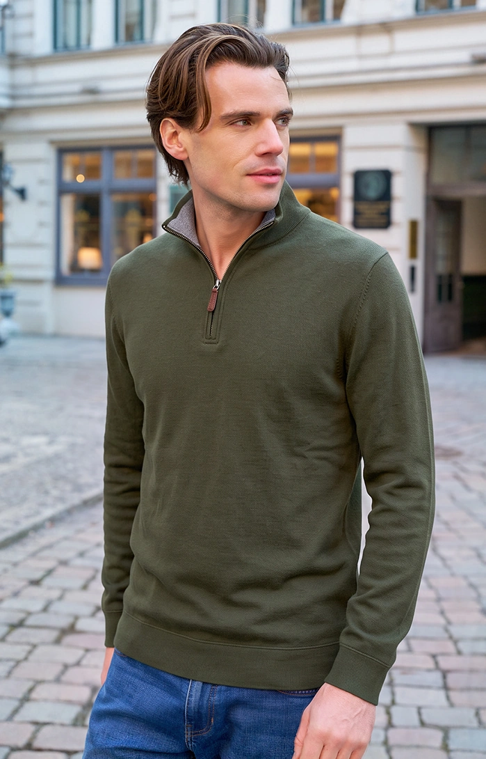 Mann trägt einen grünen Pullover und Jeans mit einer Grafik zum Mid-Season-Sale