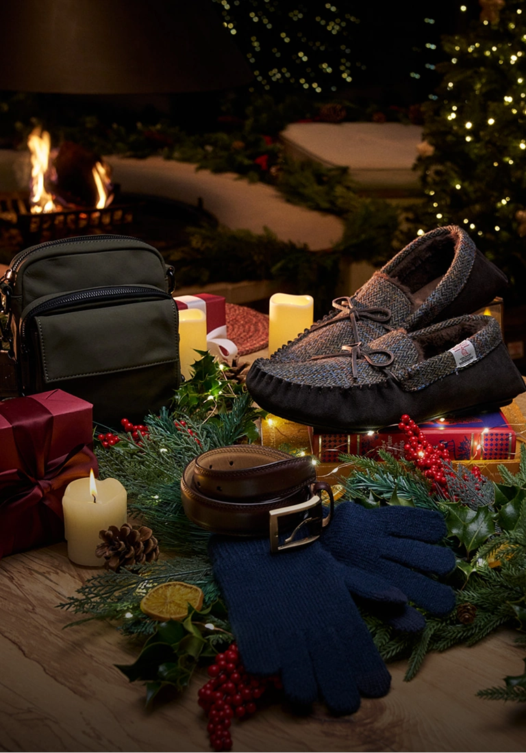 Weihnachtsgeschenke mit einer Tasche, Schuhen, Schals und einer blauen Strickmütze, arrangiert mit festlichem Grün und Kerzen